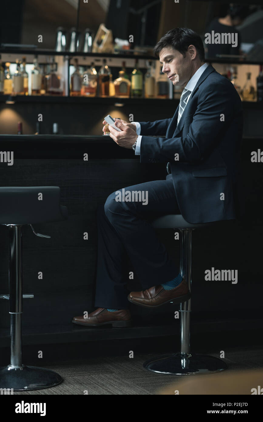Businessman using mobile phone while having whiskey Stock Photo