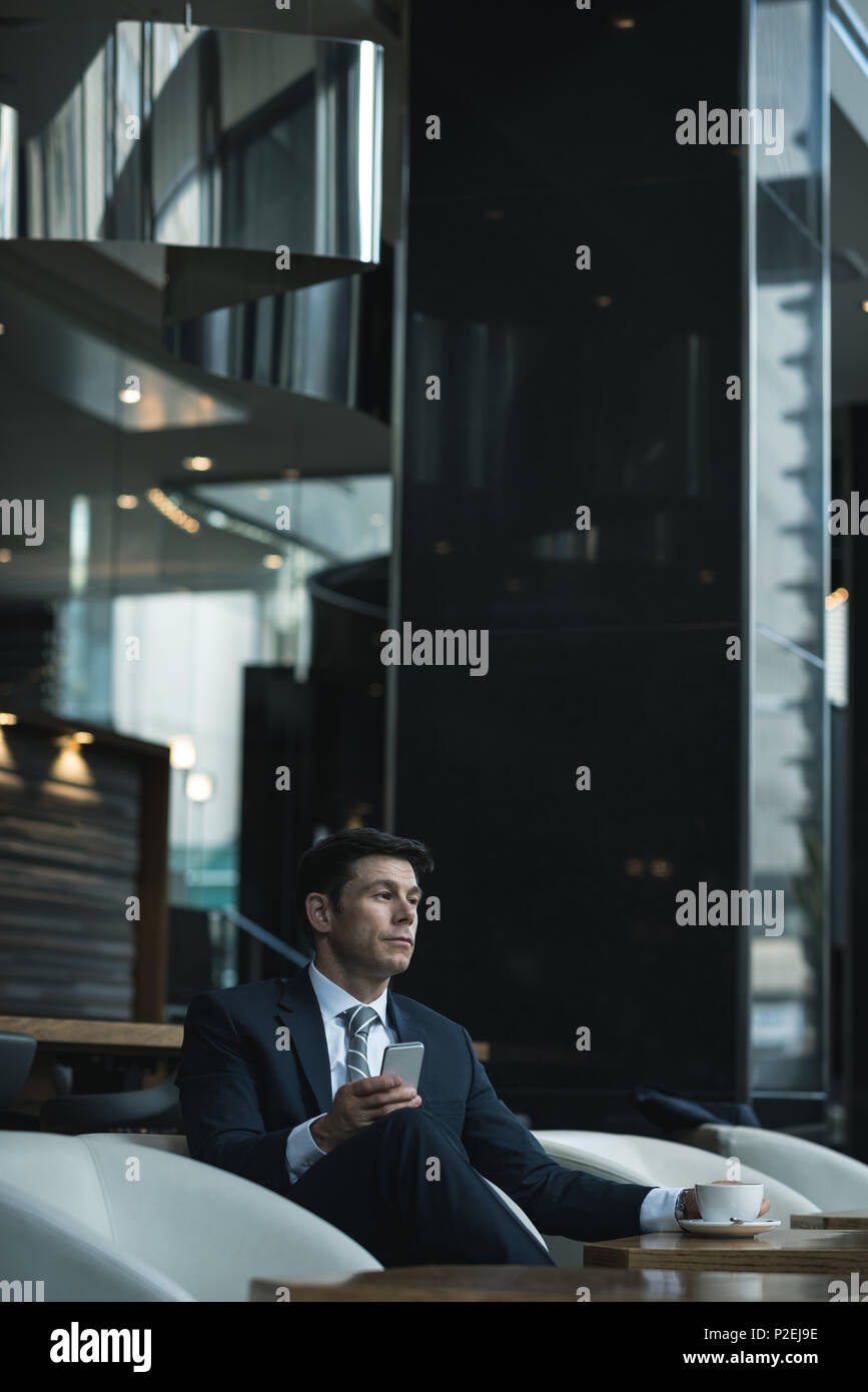 Thoughtful businessman using mobile phone while having coffee Stock Photo