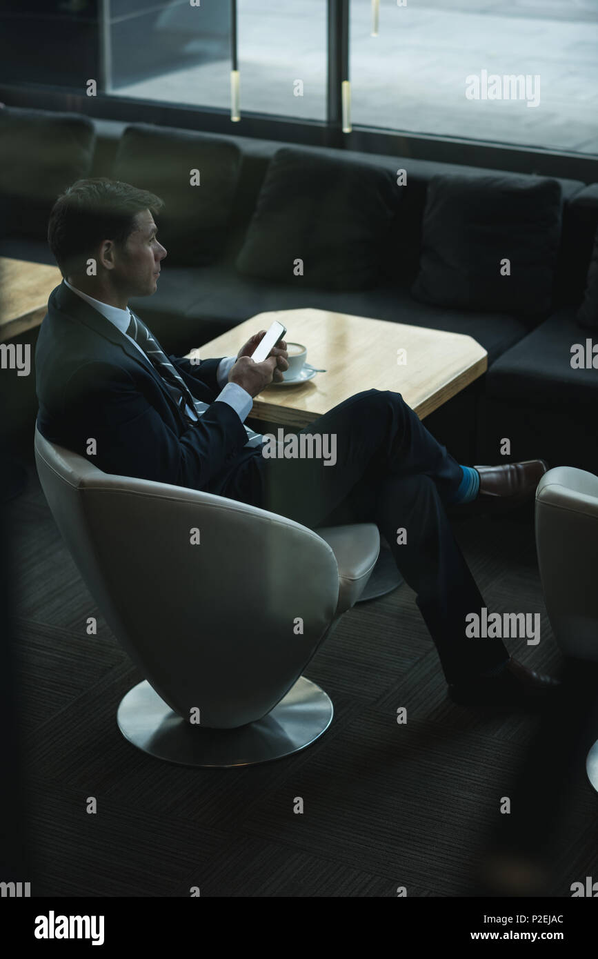 Thoughtful businessman using mobile phone while having coffee Stock Photo