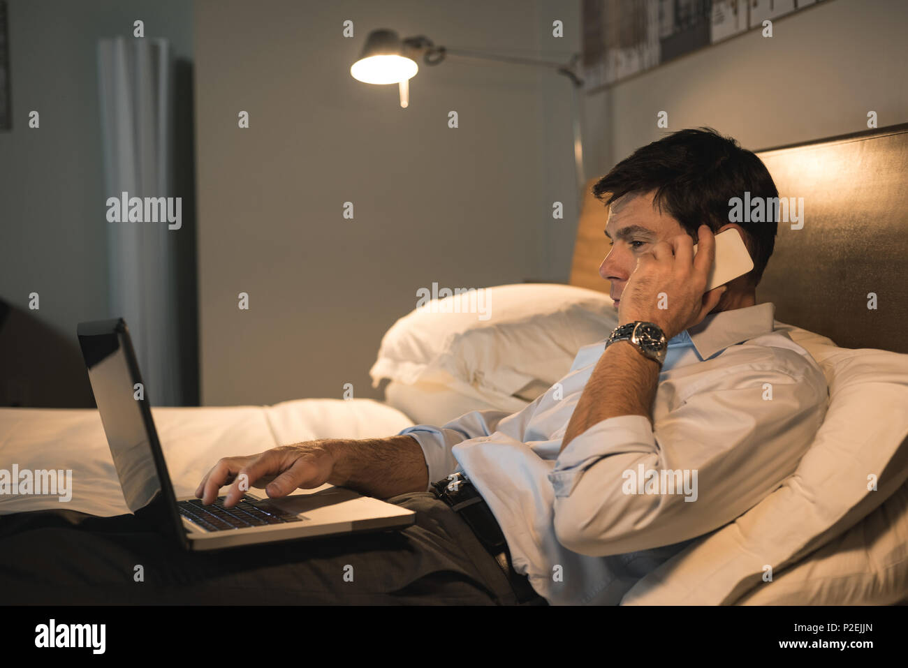 Businessman using laptop while talking on mobile phone Stock Photo