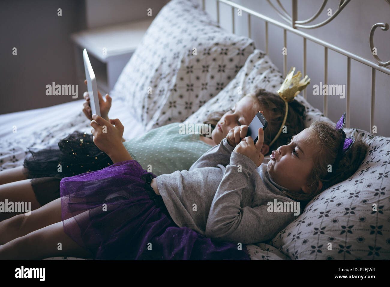 Siblings using mobile phone and digital tablet on bed Stock Photo