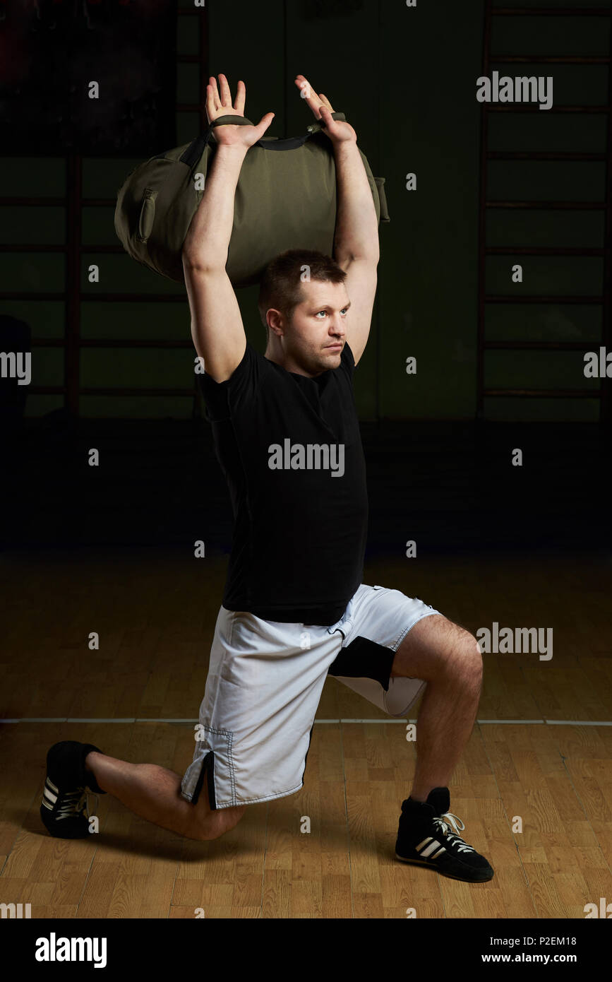 Man lifting weight bag on gym background. Caucasian male working out