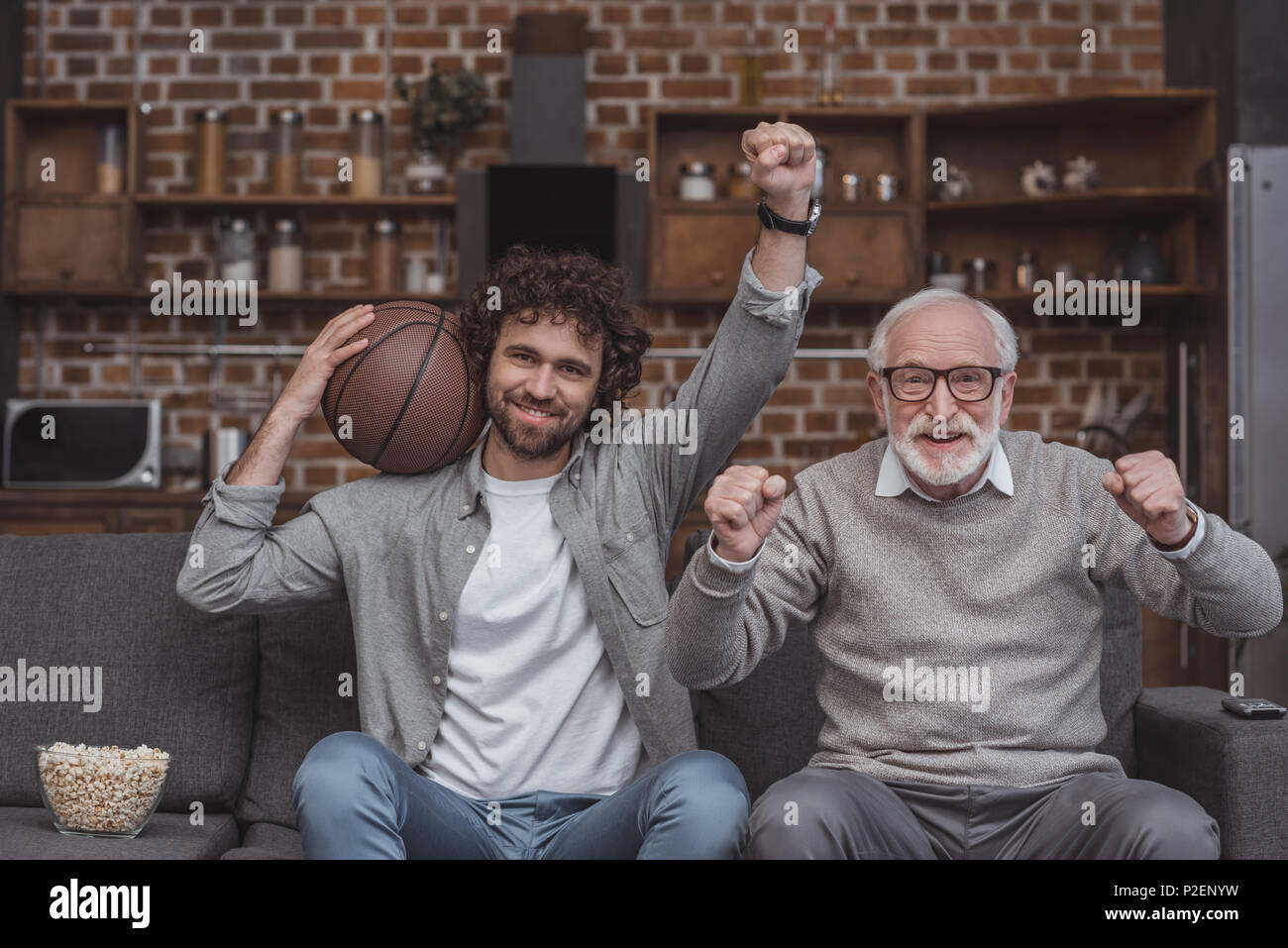 happy adult son and senior father cheering on basketball team and watching game at home Stock Photo