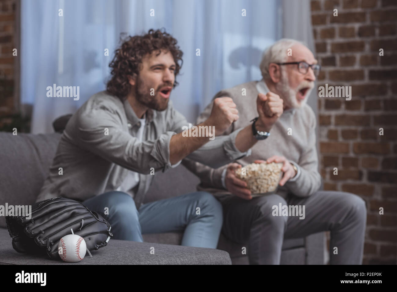 screaming adult son and senior father cheering on baseball team and watching game at home Stock Photo