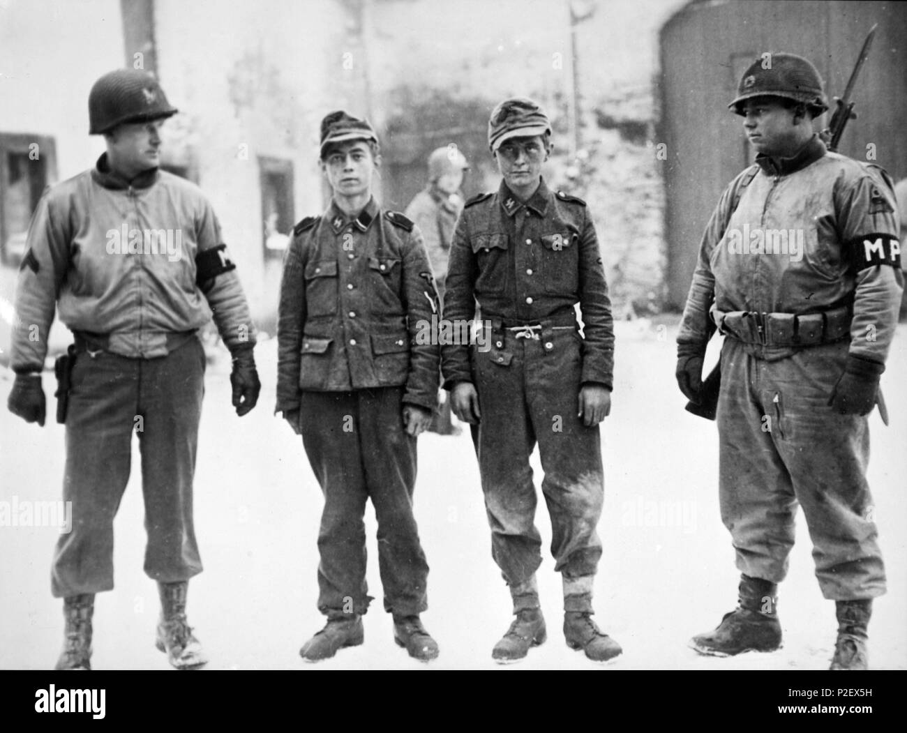 Dos soldados norteamericanos custodian a dos jóvenes prisioneros alemanes capturados en la eliminación del saliente de Bastoña. Stock Photo