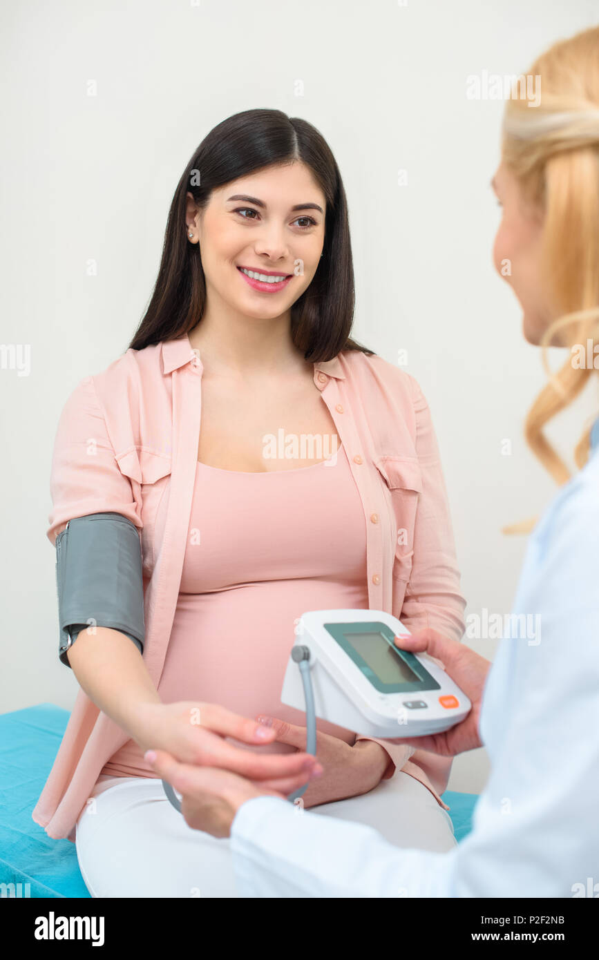 obstetrician gynecologist measuring blood pressure of smiling pregnant woman at clinic Stock Photo