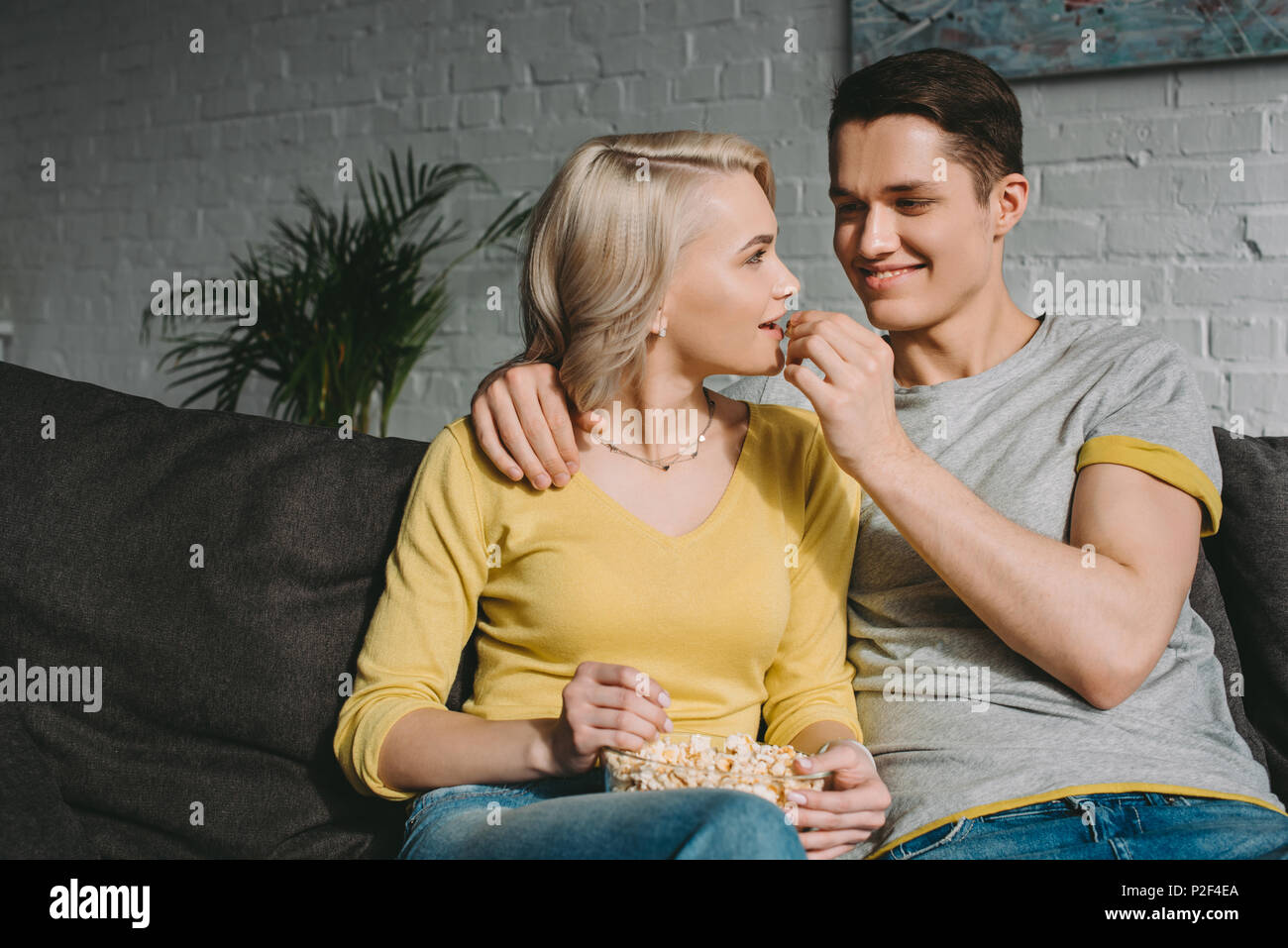 happy boyfriend feeding girlfriend with popcorn on sofa Stock Photo Alamy