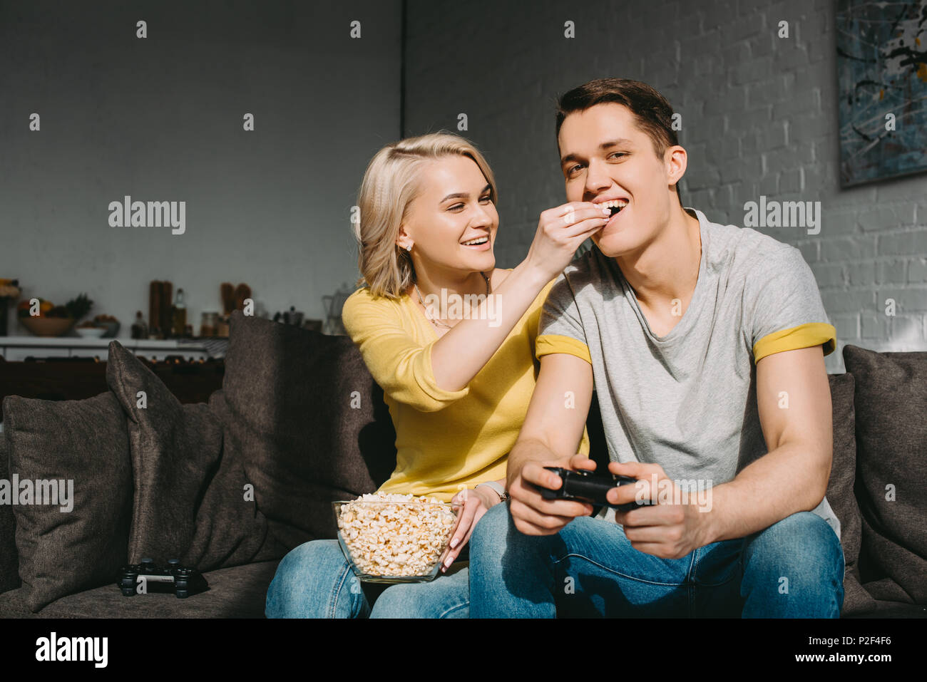 smiling girlfriend feeding boyfriend with popcorn at home Stock Photo