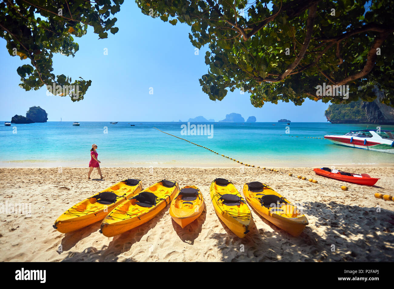 Woman in pink dress walking on the Phranang beach with yellow kayak boat in Thailand Stock Photo