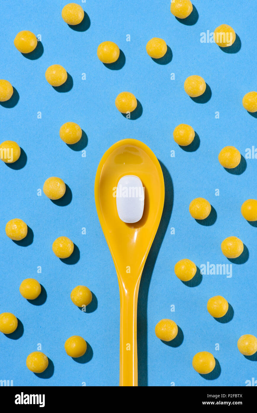 top view of yellow plastic spoon with white pill surrounded with pills on blue Stock Photo