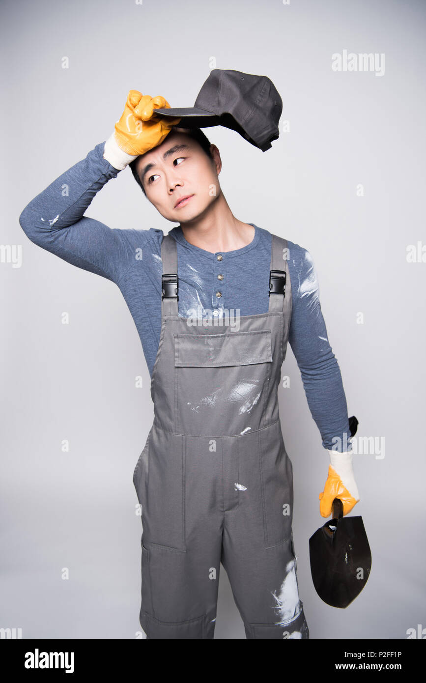 Young construction worker in overalls and safety gloves wiping the ...