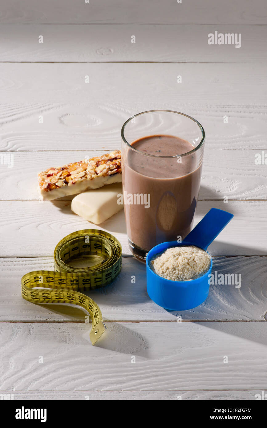chocolate protein shake with energy bars and measuring tape on white wooden table Stock Photo