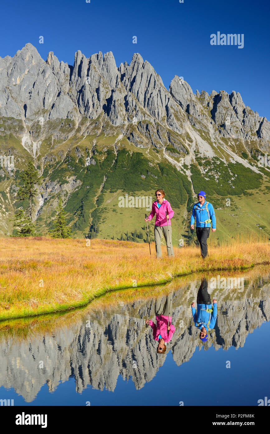 Man and woman hiking near a mountain lake with Mandlwand ridge at Hochkoenig in the background, Berchtesgaden range, Salzburg, A Stock Photo