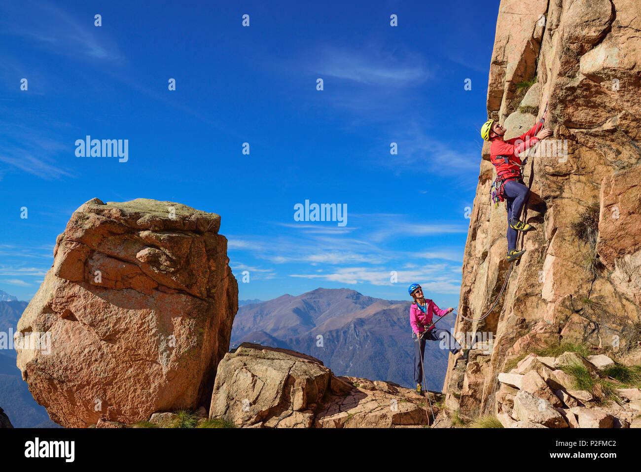 Man climbing on red Granite rock is being belayed by woman, Mottarone, Piedmont, Italy Stock Photo
