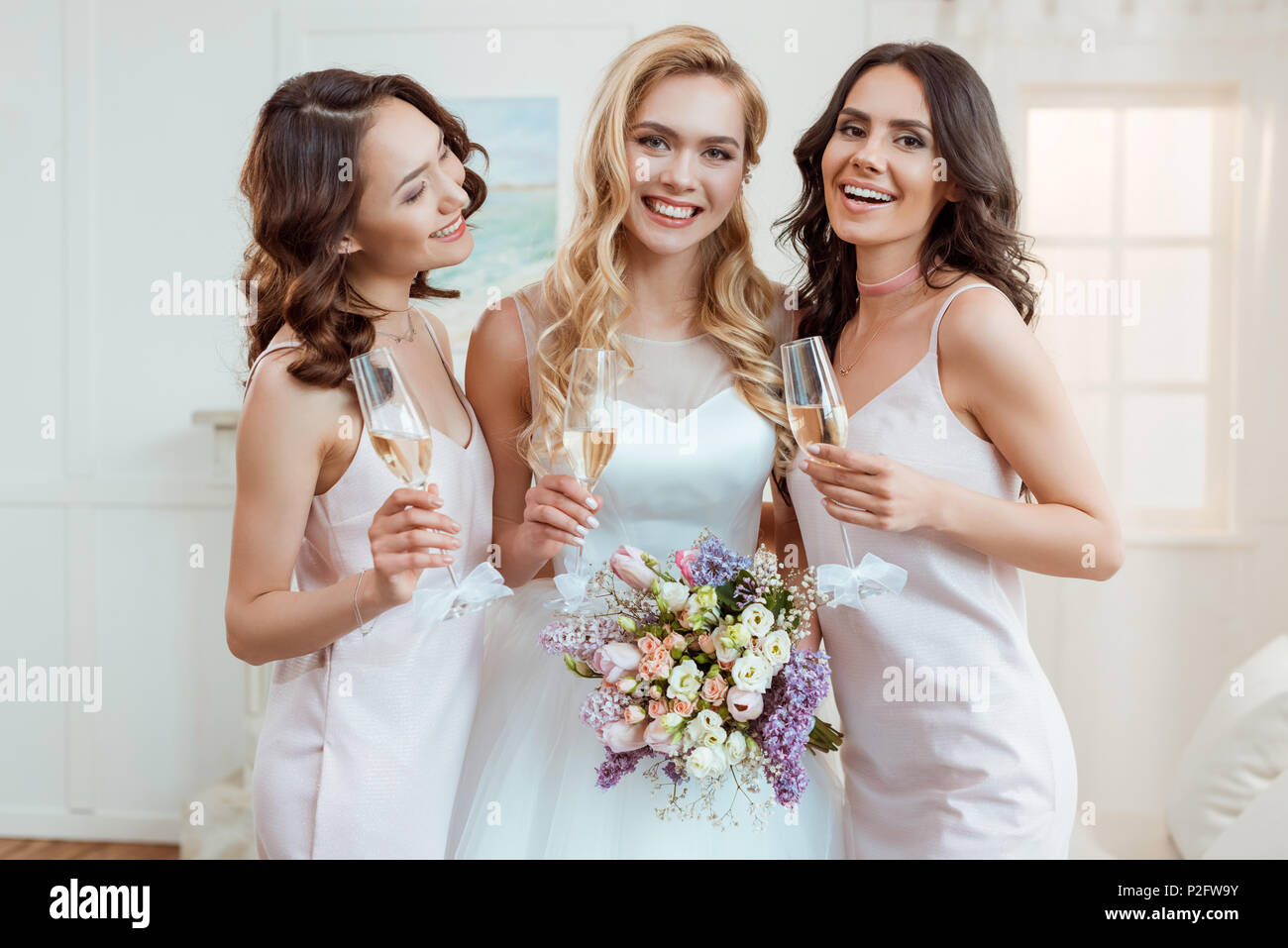 beautiful bride with bridesmaids drinking champagne in dresses Stock