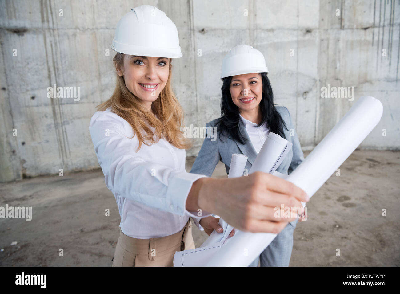 Two attractive smiling architects holding blueprint while working at construction site Stock Photo