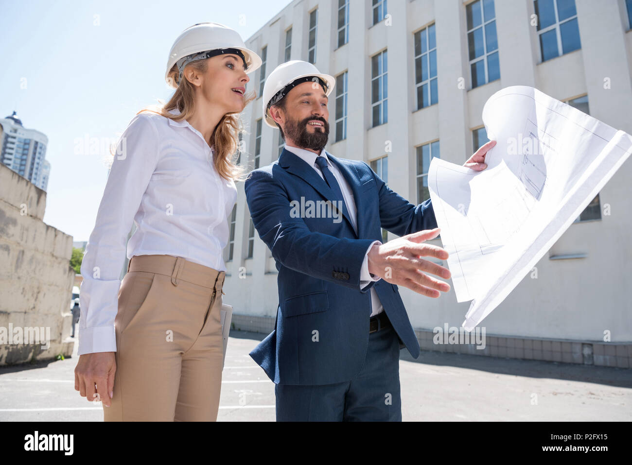 Two smiling architects holding blueprint and discussing project while working together Stock Photo