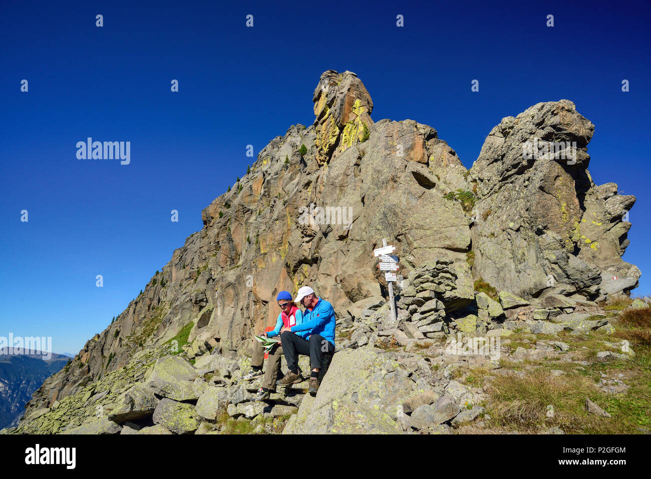 Two hikers sitting beneath a rock spire and looking at a map, Trans-Lagorai, Lagorai range, Dolomites, UNESCO World Heritage Sit Stock Photo
