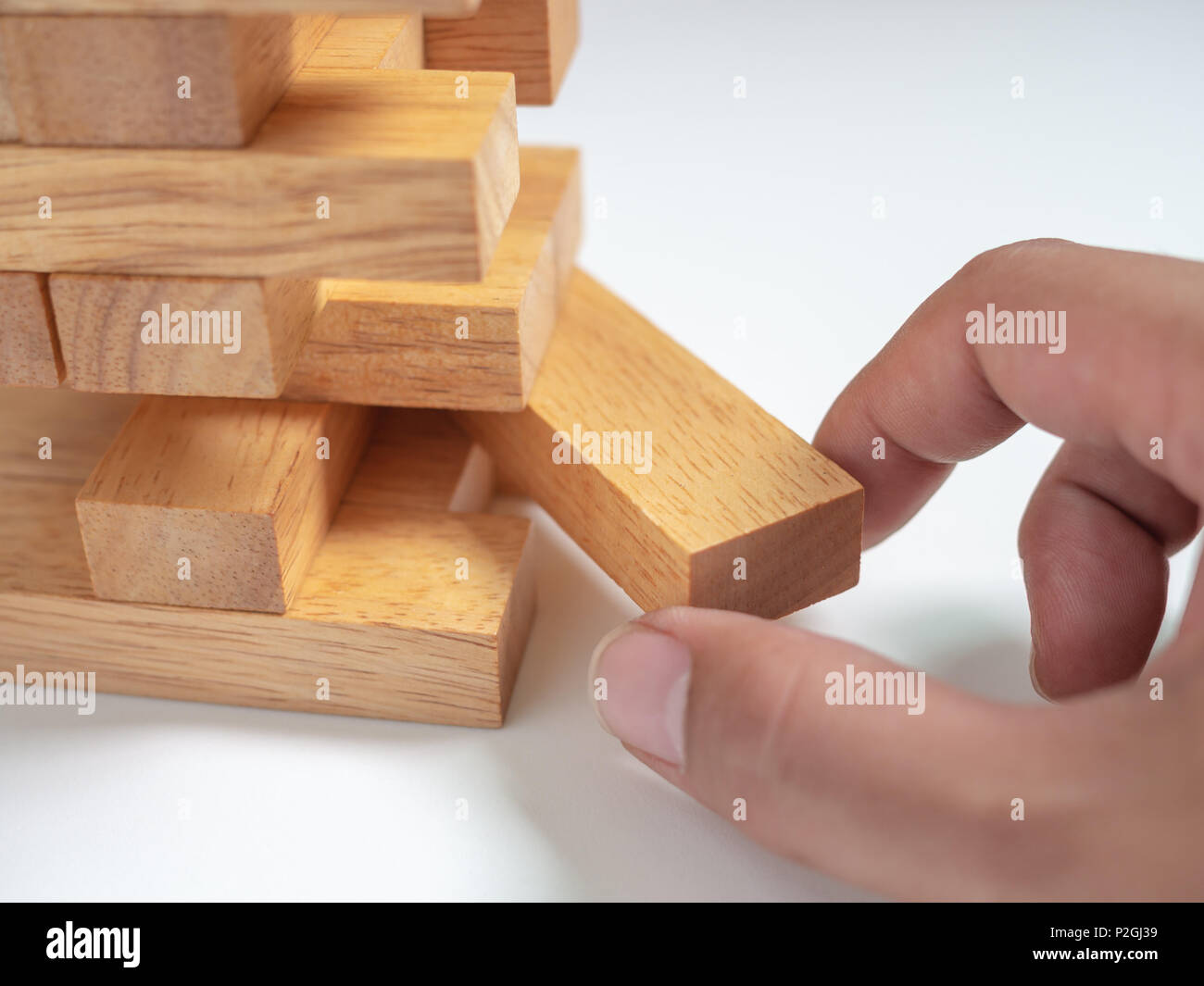 Hand Move out The Block Playing Tumble Tower Wooden Block Game on White Background. Business Concept Stock Photo