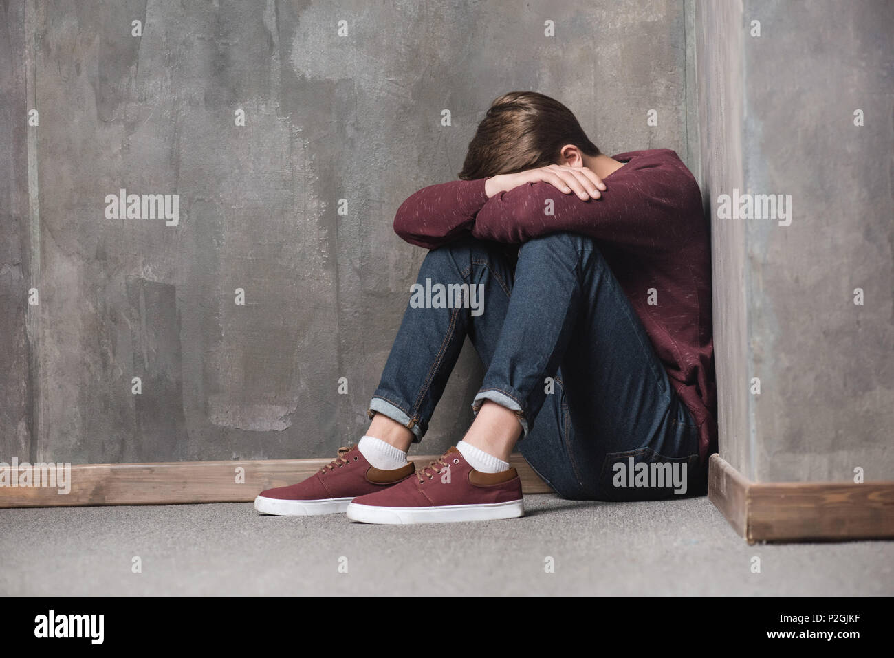 Depressed teenage boy sitting on floor with head in hands Stock Photo ...