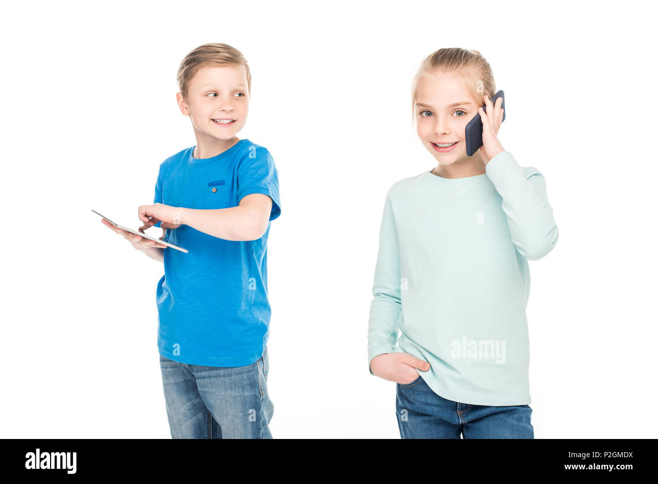 smiling little boy using digital tablet and looking at girl talking on smartphone isolated on white Stock Photo