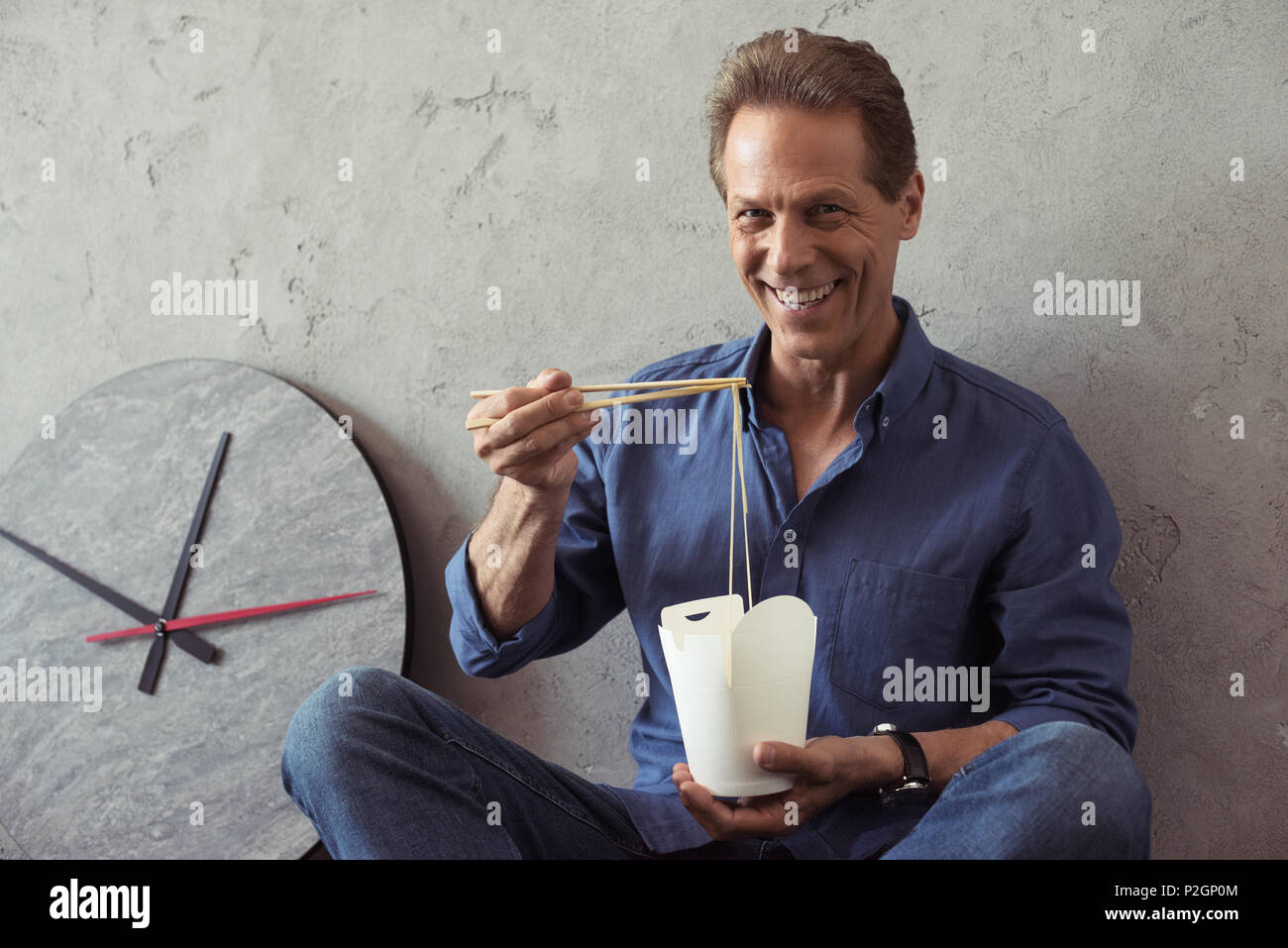smiling middle aged man eating noodles and looking at camera Stock Photo