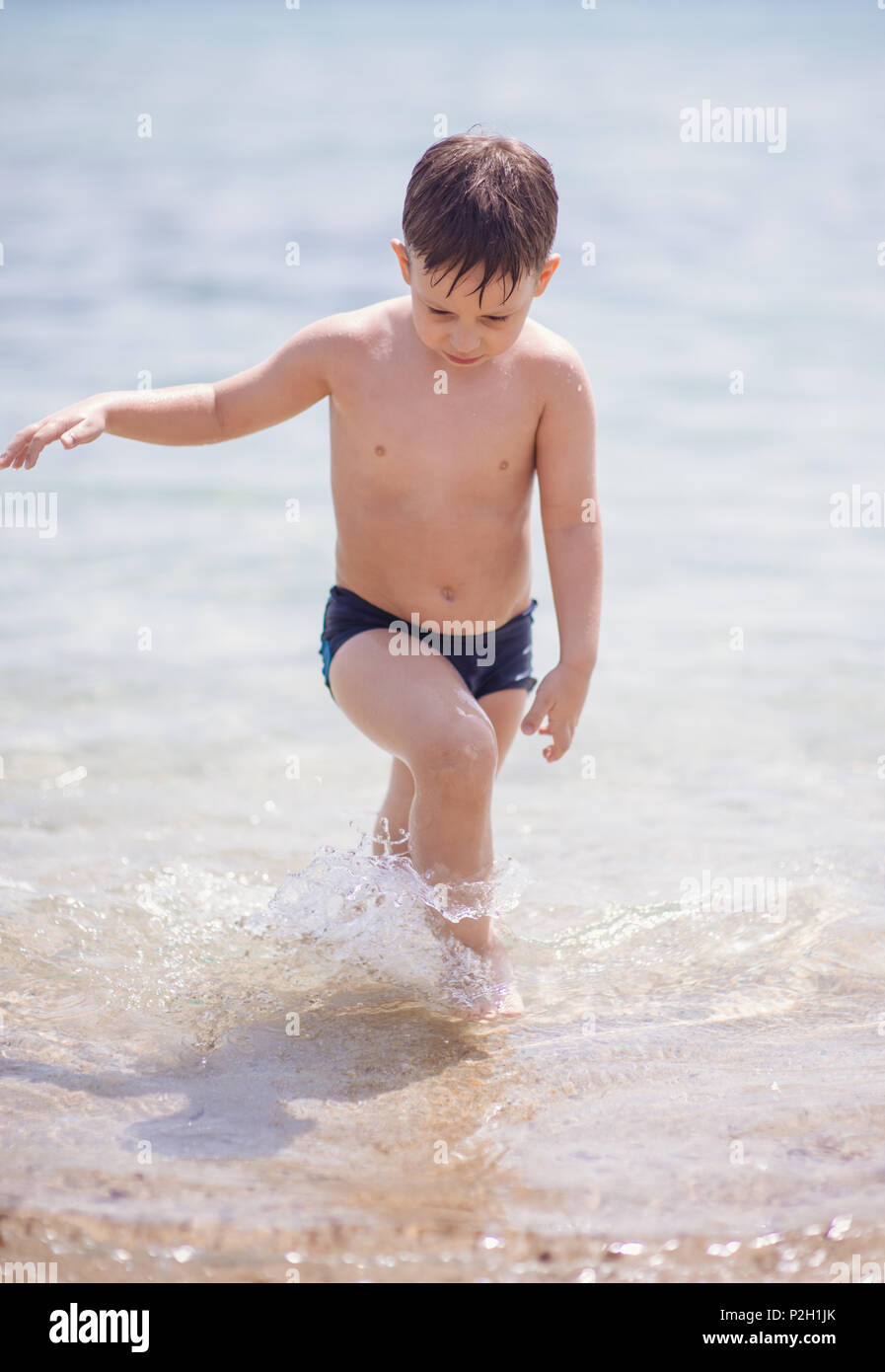 Adorable boy that wears black swimsuit is standing in the shallow water on  the beach Stock Photo - Alamy