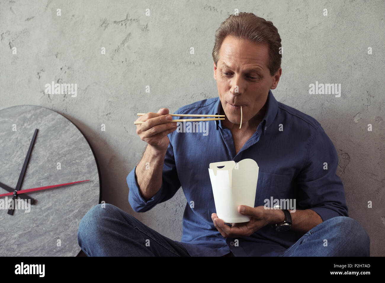 casual middle aged man eating noodles with chopsticks Stock Photo
