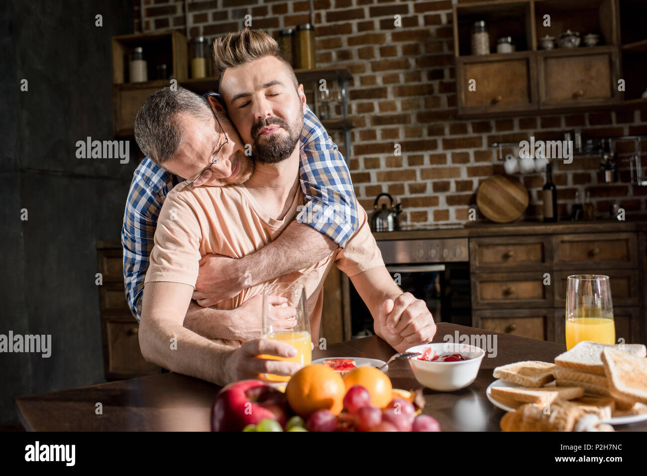 Happy gay couple hugging while having breakfast at home Stock Photo - Alamy