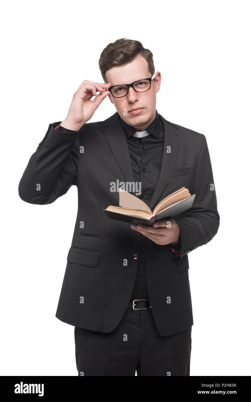 young priest in black suit reading scripture book and looking at camera isolated on white Stock Photo