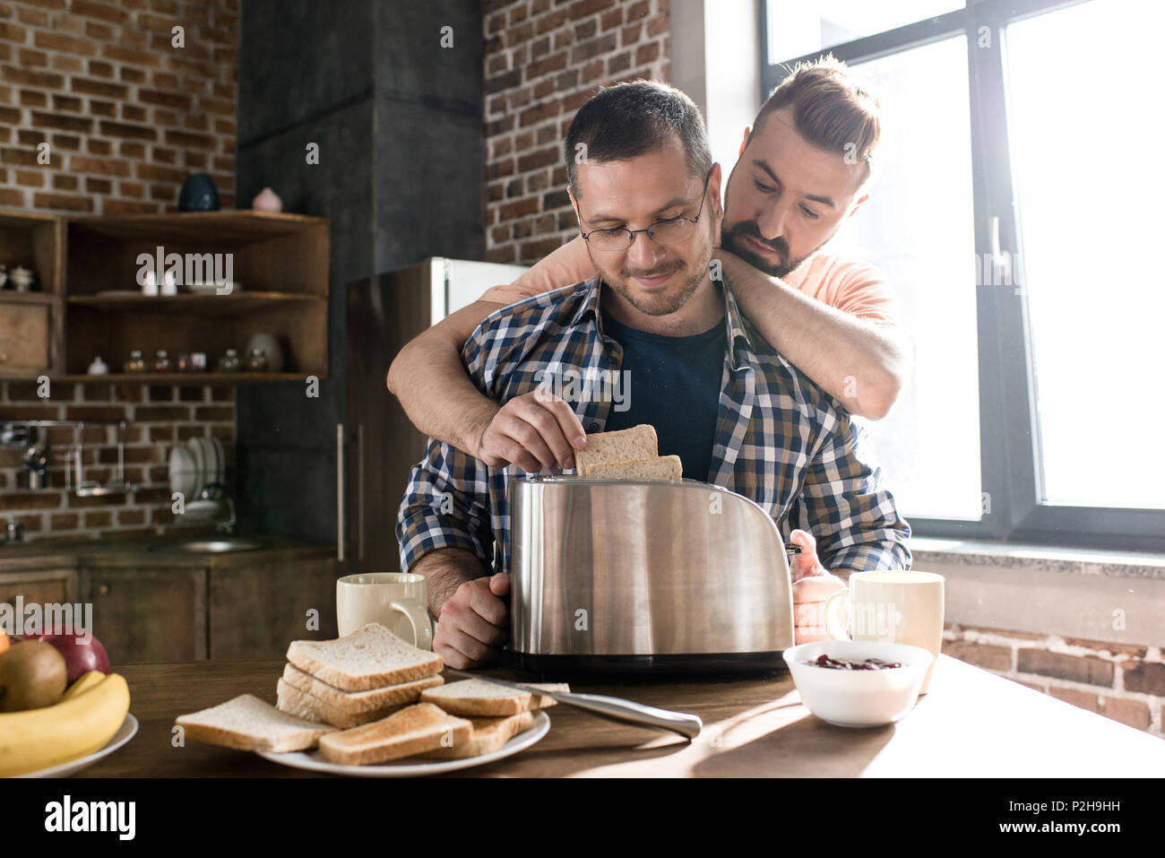 Happy gay couple hugging and making toasts together at morning Stock