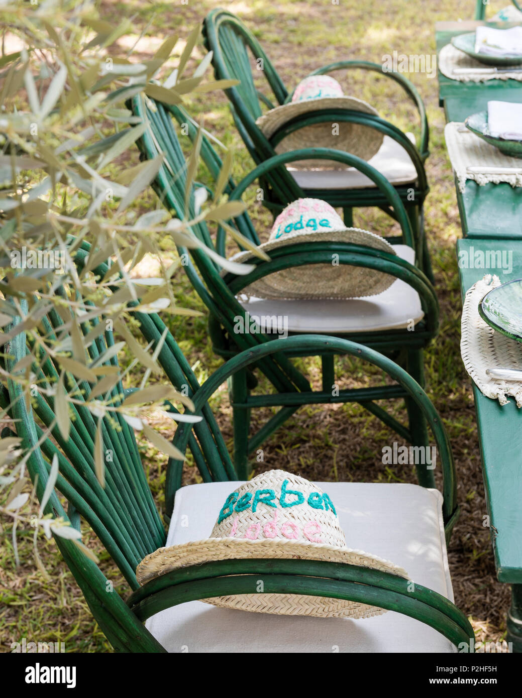 Berber Lodge straw hats on green chairs set at outdoor dining table Stock Photo