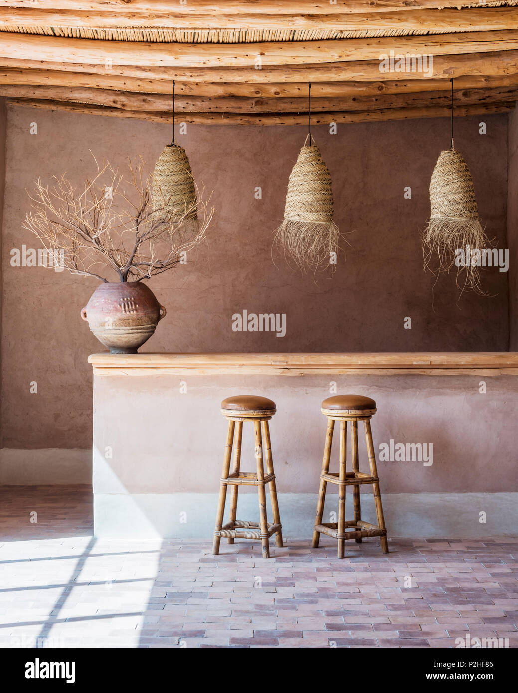 Rattan lanterns hang above counter with bamboo bar stools in bar with wood ceiling and terracotta floor. The antique pot comes from east africa Stock Photo