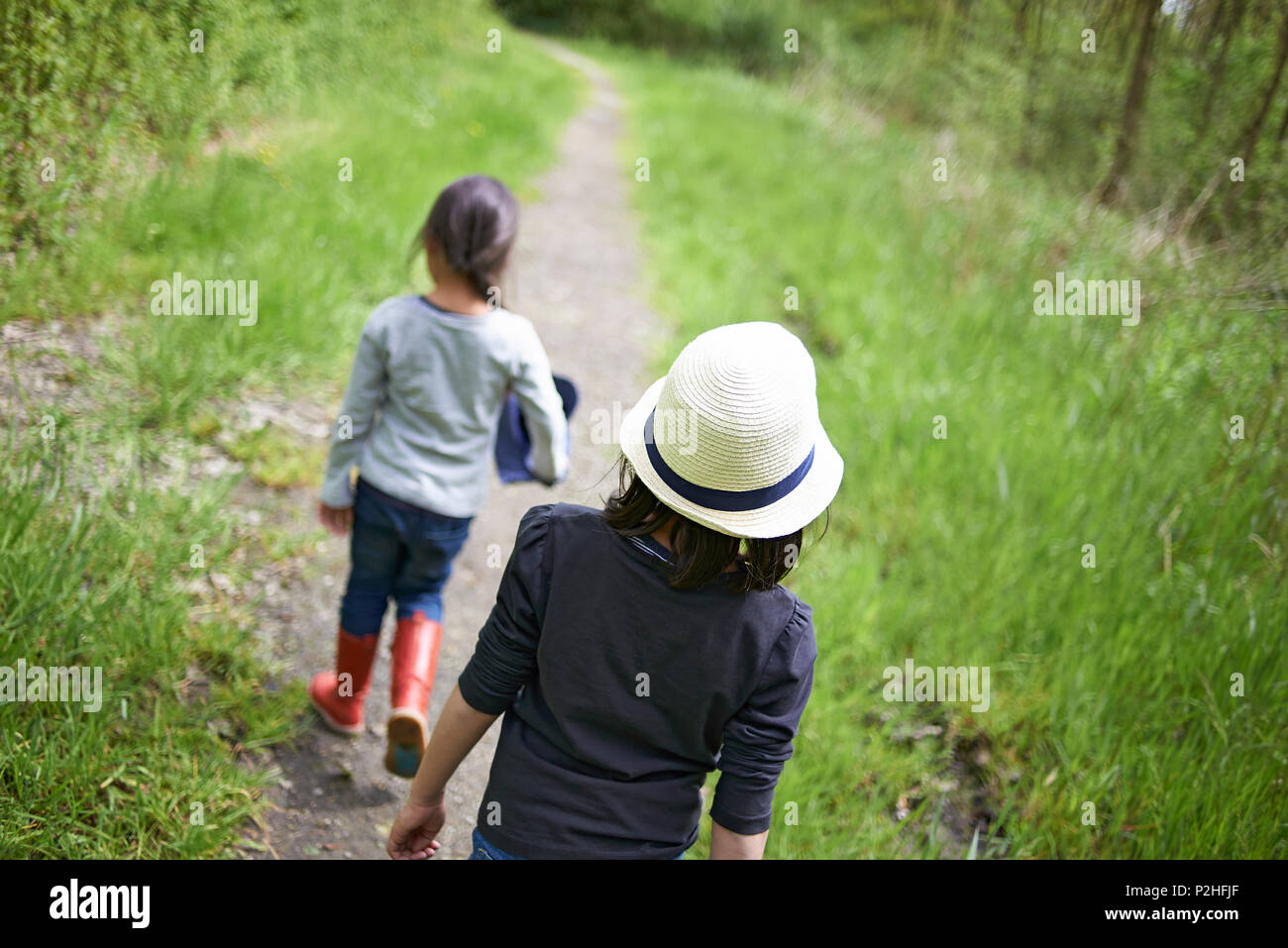 Two young Asian sisters walking on a small path in a forest surrounded ...