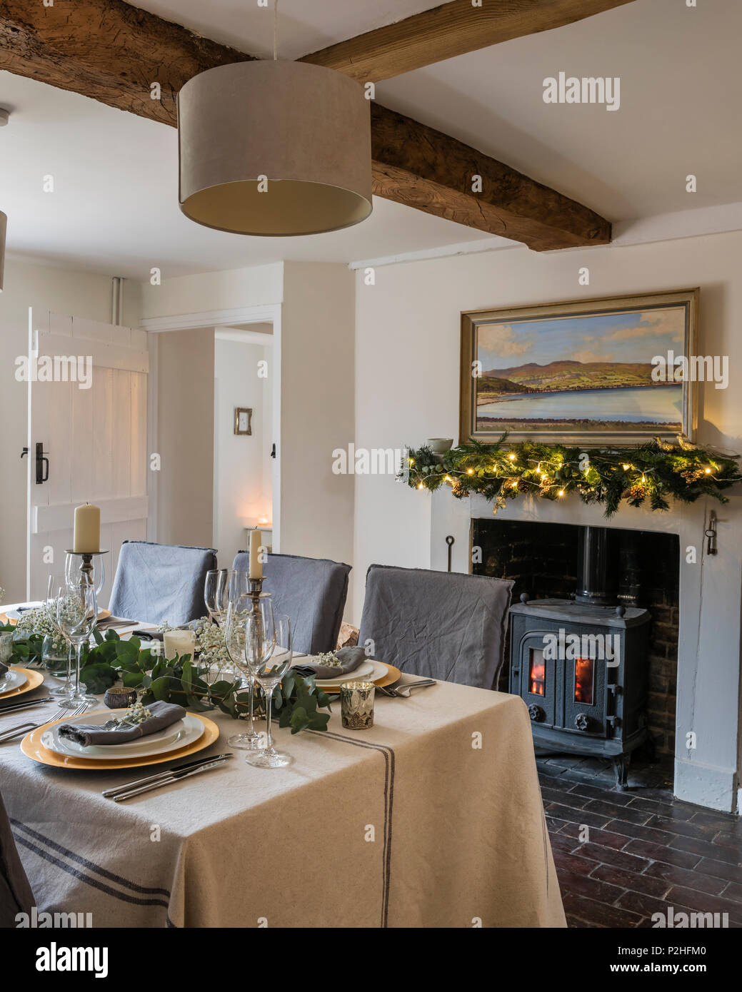 Sam McLarnon landscape painting above fireplace in cosy cottage dining room. The table linen is from Maison Brocante Stock Photo