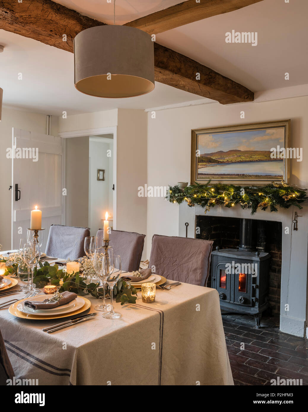 Sam McLarnon landscape painting above fireplace in cosy cottage dining room. The table linen is from Maison Brocante Stock Photo