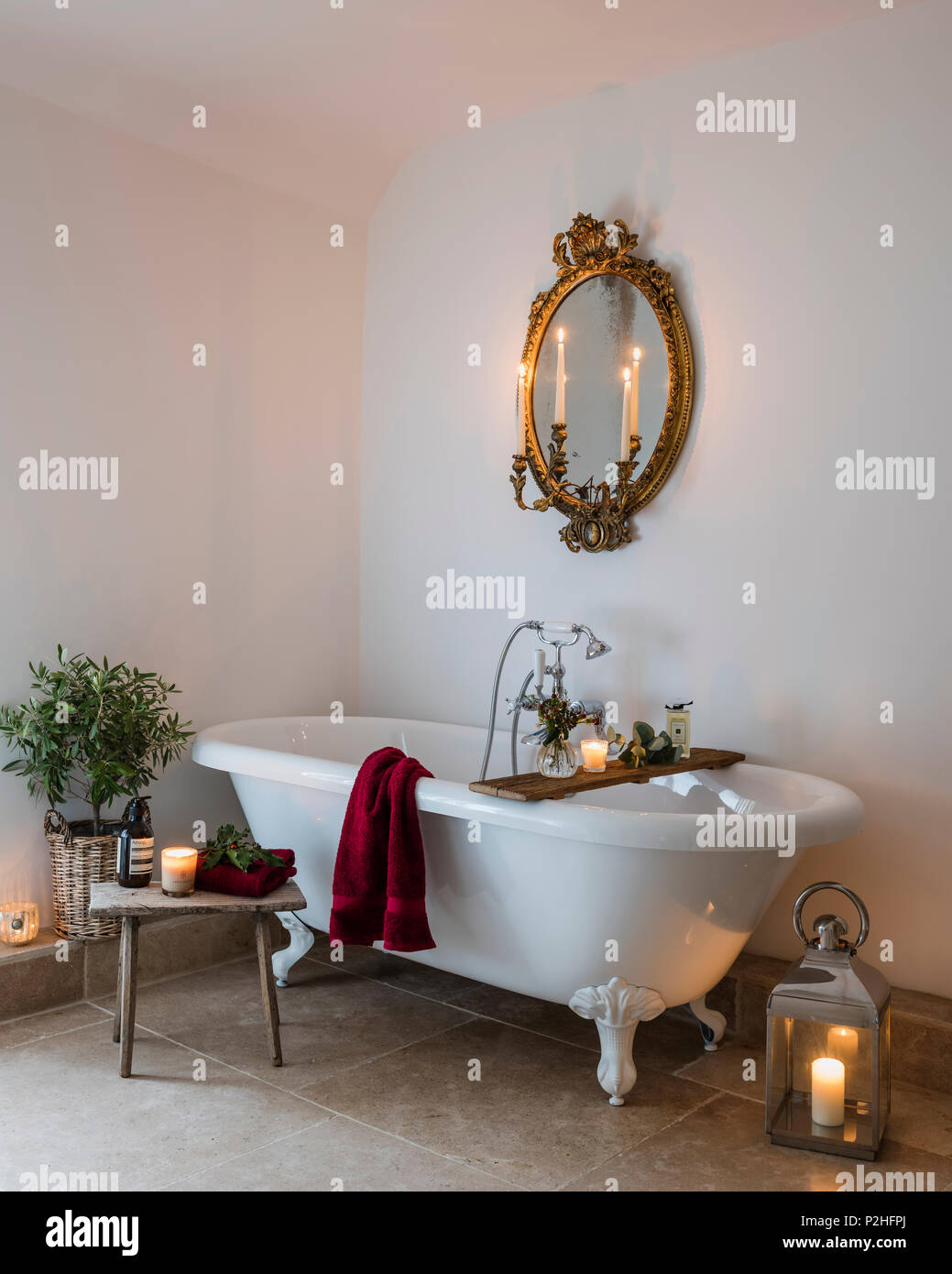 Antique gilt mirror in bathroom with free standing bath tub, limestone floor and small wooden milking stool. Stock Photo