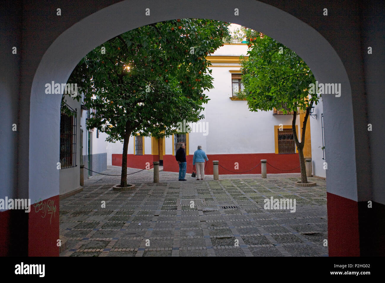 A small square, Calle Susona, in Barrio de Santa Cruz, Sevilla, Andalusia, Spain, seen through an archway from Calle Agua Stock Photo