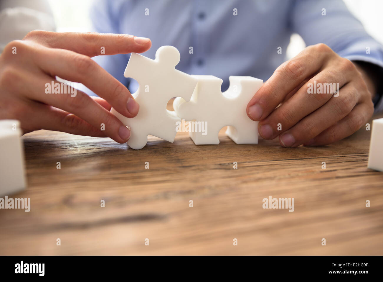 Close-up Of Two Businesspeople White Jigsaw Pieces Over Wooden Desk Stock Photo