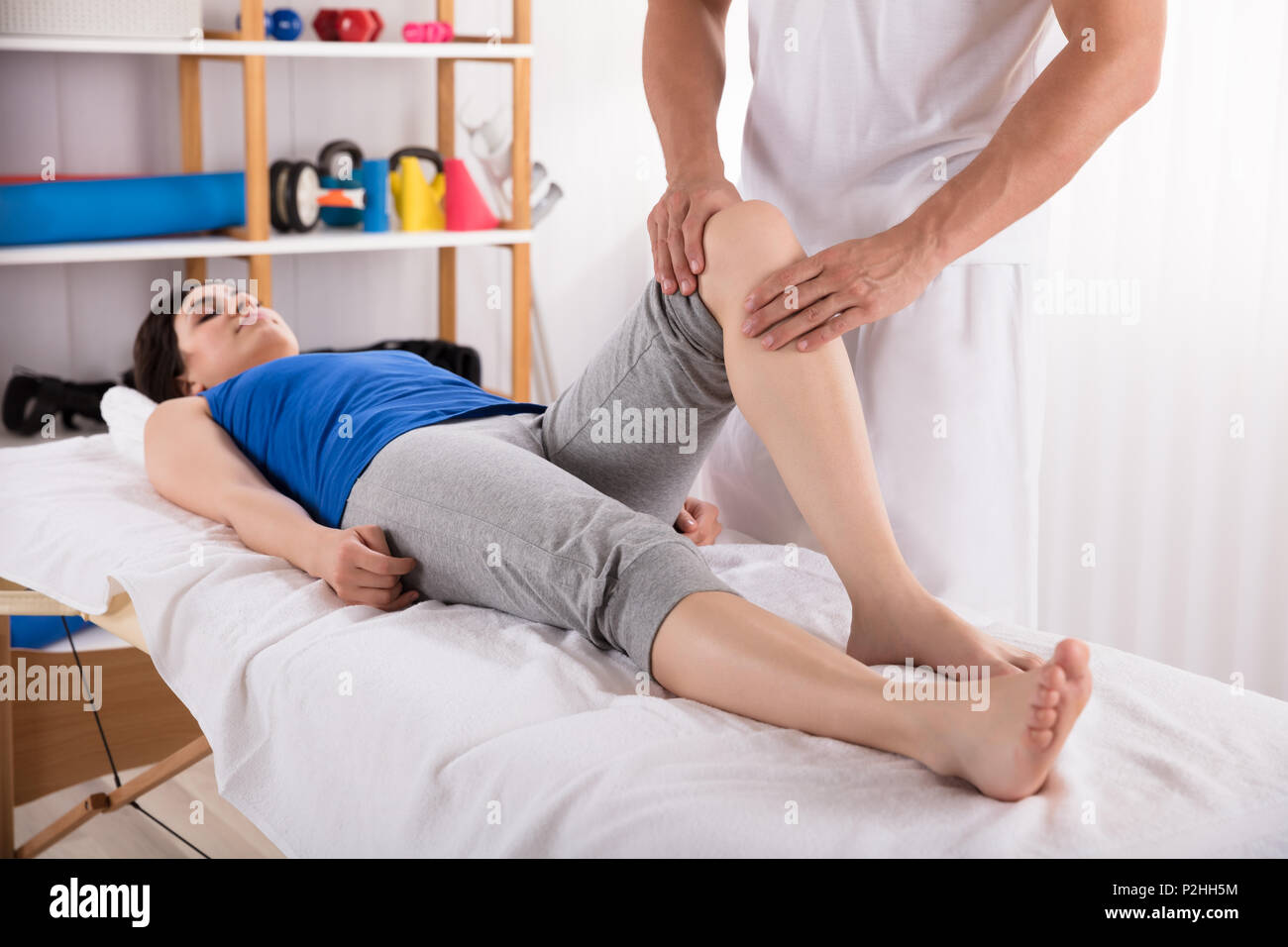 Woman Lying On Bed Receiving Leg Massage By Physiotherapist Stock Photo