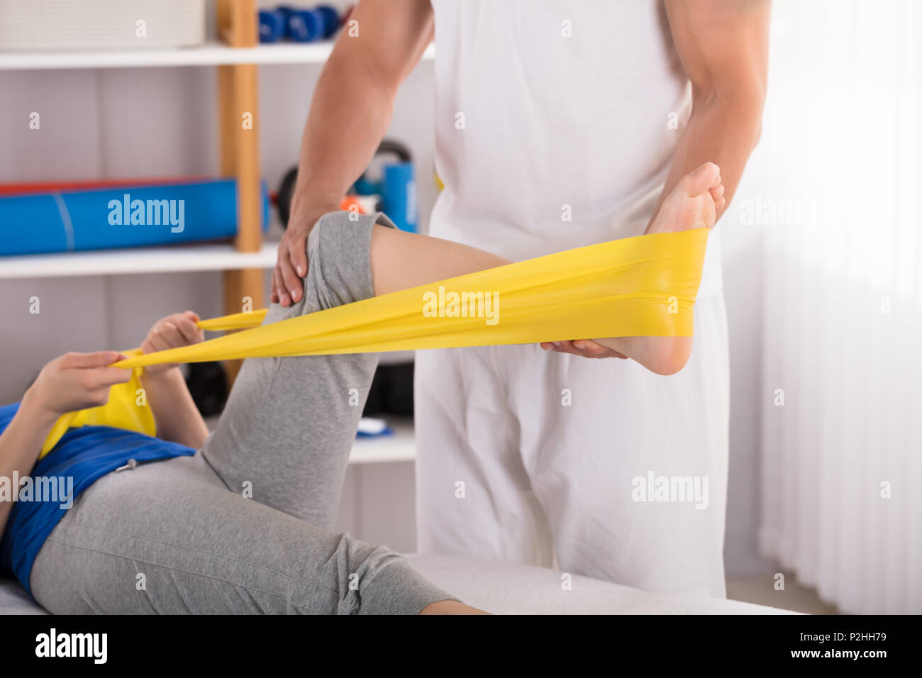 Physiotherapist Giving Leg Treatment To Woman With Yellow Exercise Band Stock Photo