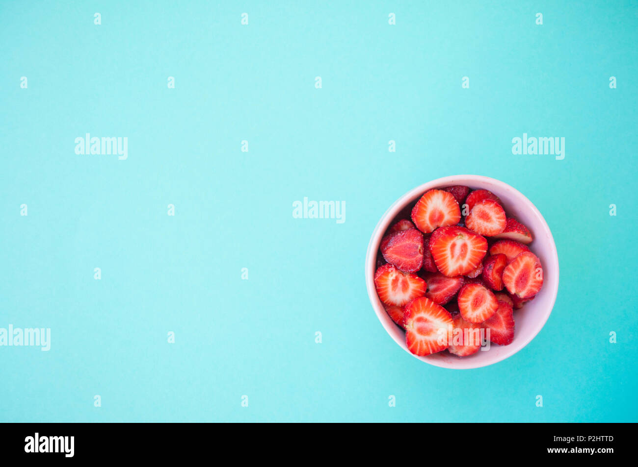 A pink bowl full of beautiful fresh juicy strawberries on bright blue ...