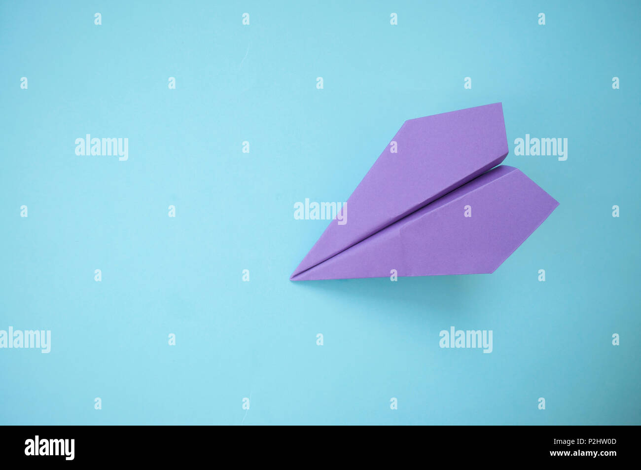 Flat lay of purple paper plane on pastel blue background with text space. Stock Photo