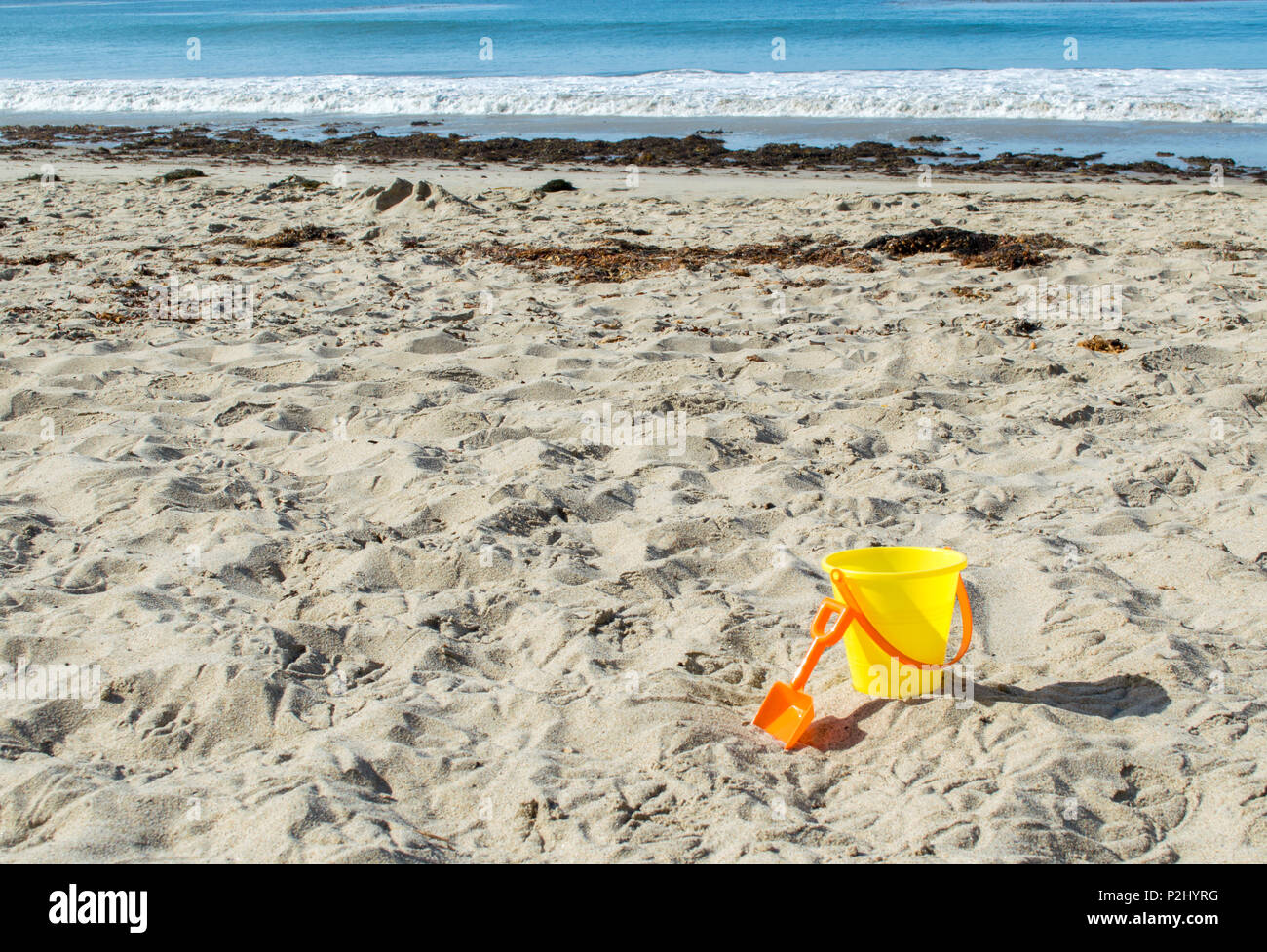 yellow plastic sand pail with orange shovel in the sand at the beach on