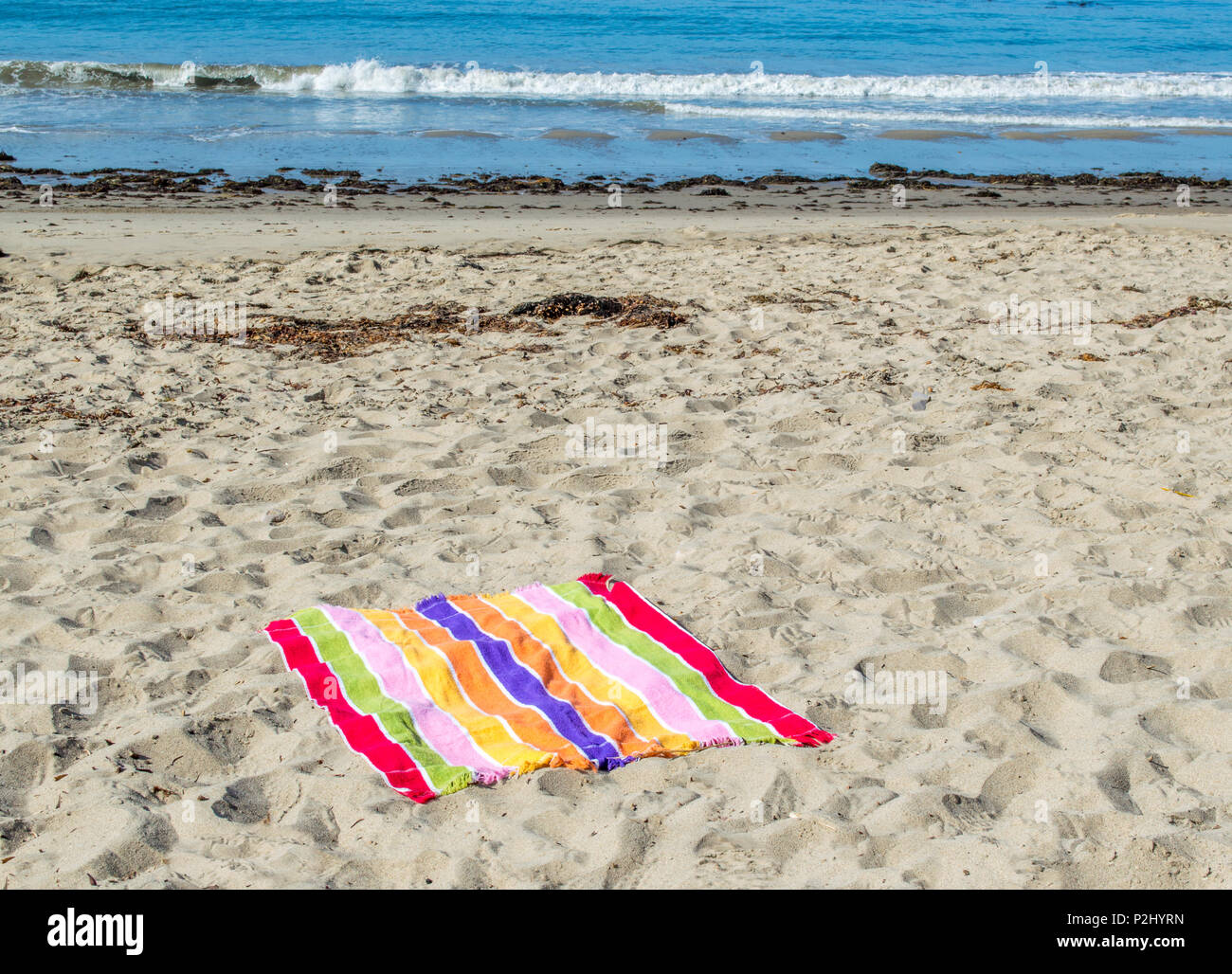 colorful striped beach towel on an empty beach with the ocean in the distance on a sunny summer day Stock Photo