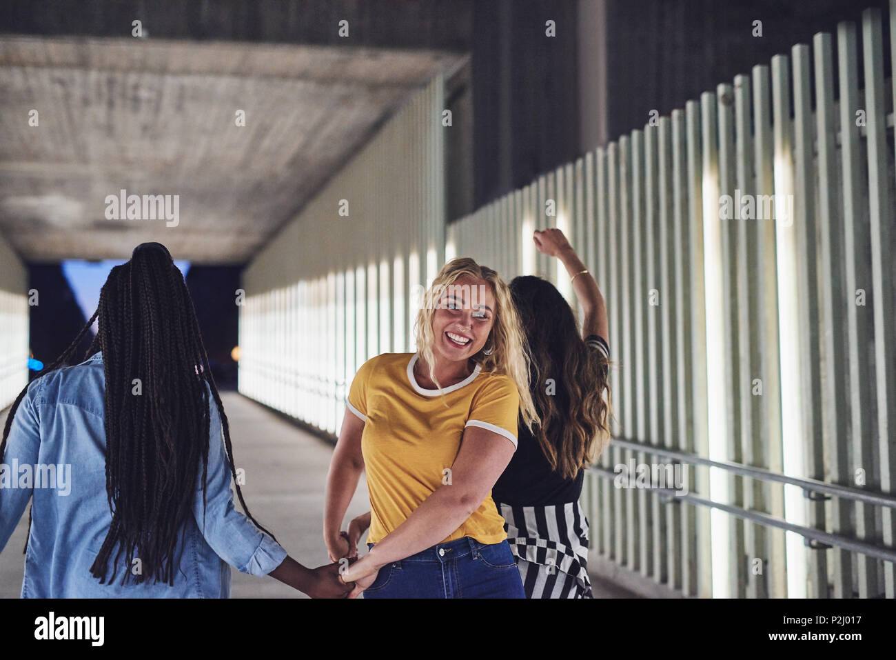 Laughing young woman walking hand in hand with two female friends ...