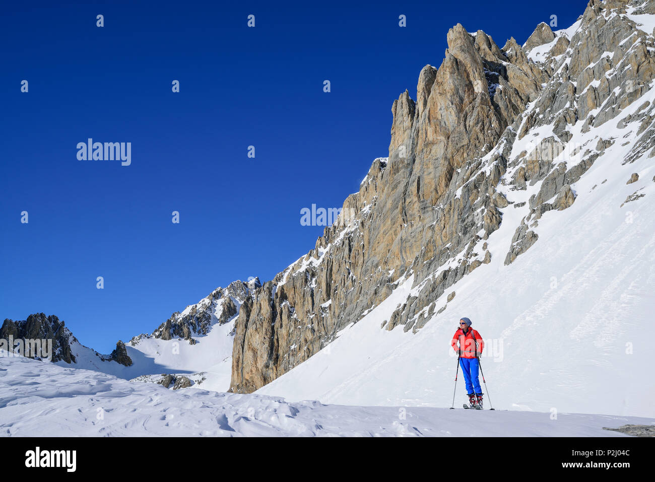 Woman back-country skiing standing beneath rock wall of Monte Sautron, Valle Maira, Cottian Alps, Piedmont, Italy Stock Photo