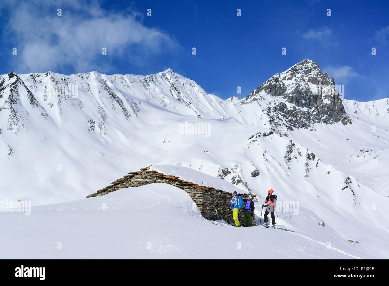 Three persons back-country skiing standing in front of alpine hut, Tete dell'Autaret and Pelvo di Ciabriera in background, Monte Stock Photo