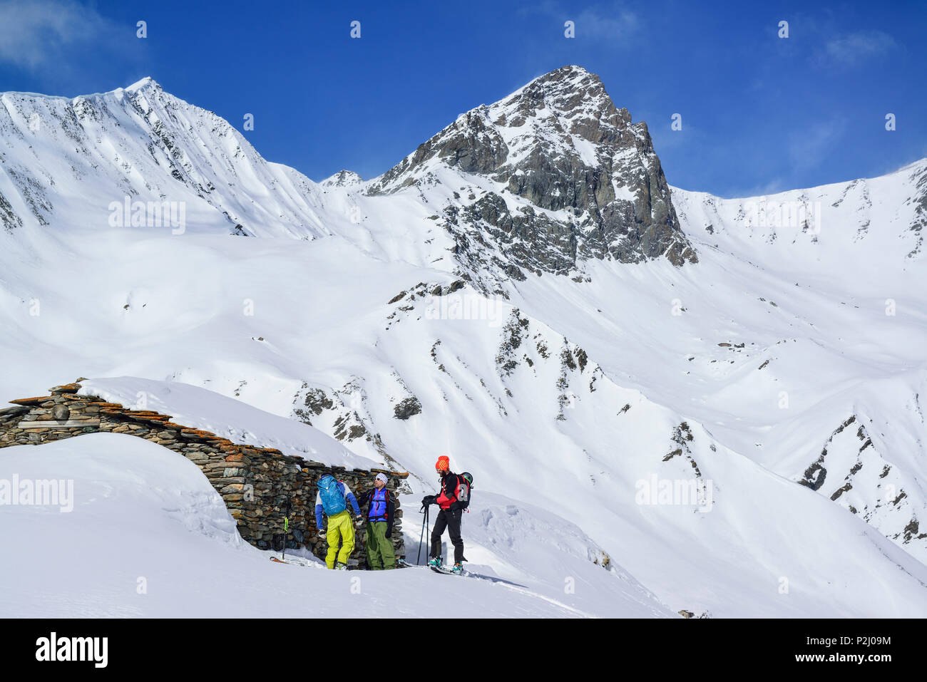 Three persons back-country skiing standing in front of alpine hut, Tete dell'Autaret and Pelvo di Ciabriera in background, Monte Stock Photo