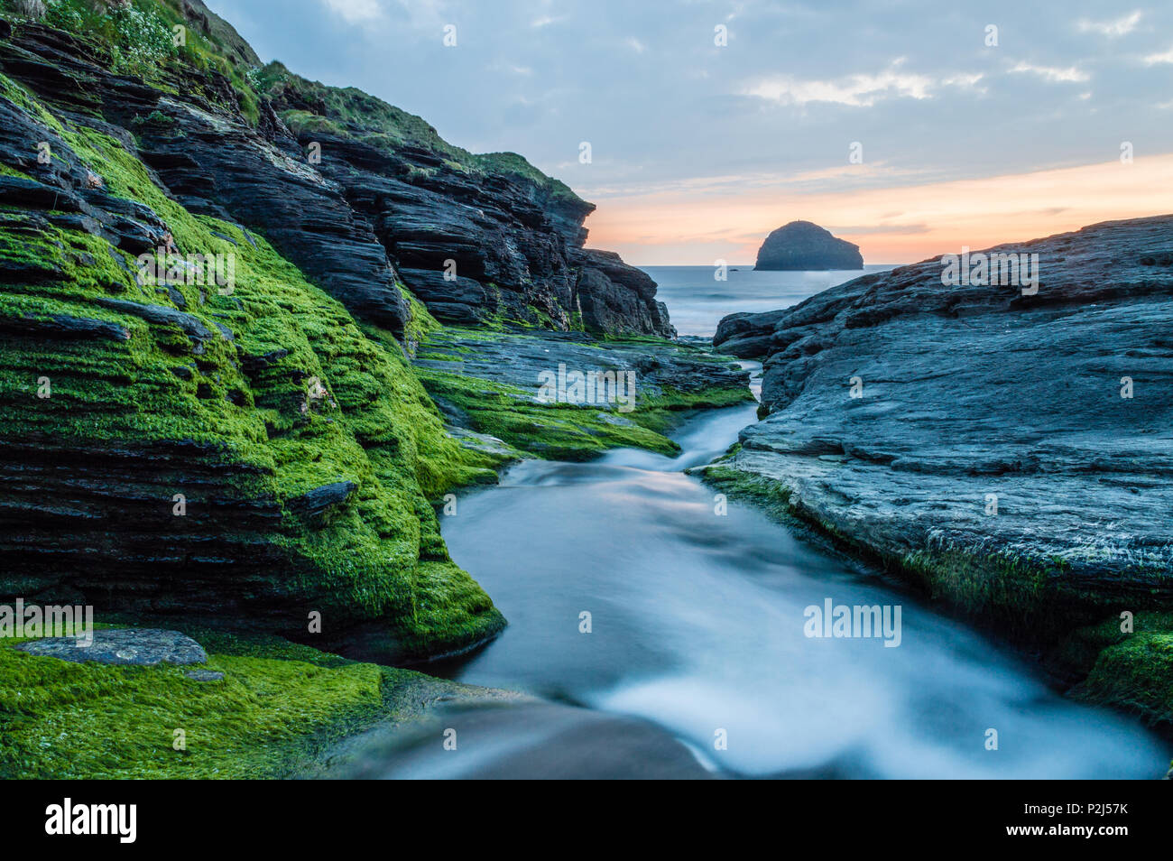 Stream leading down the rocks to the sea at Trebarwith strand with orange sly and gull rock, North Cornwall Stock Photo